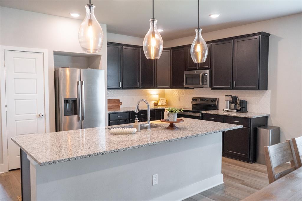 7909 Townsend Drive Waco, TX 76708 - Photo 7 of 22 Kitchen featuring a large island with a stone-finish countertop, dark wood-finish cabinetry, stainless steel appliances, and wood-finish flooring