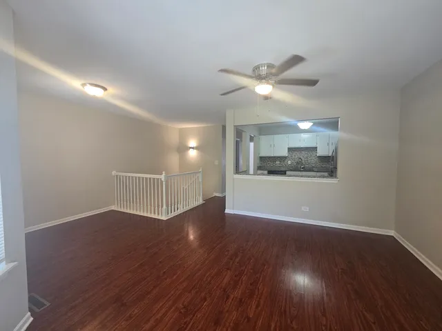 a view of an empty room with wooden floor and a ceiling fan