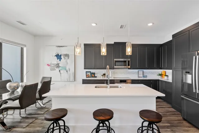 a living room with stainless steel appliances kitchen island granite countertop a dining table chairs and a refrigerator