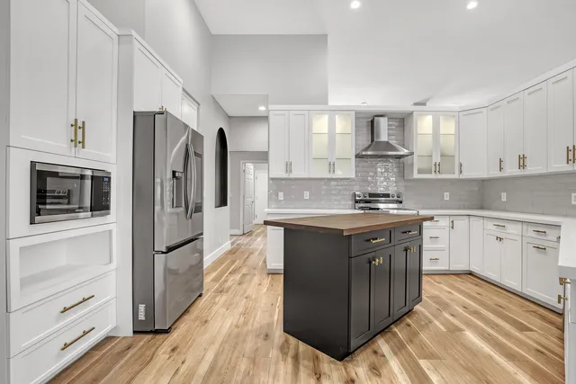 a kitchen with stainless steel appliances granite countertop a refrigerator a sink dishwasher a stove and white countertops with wooden floor