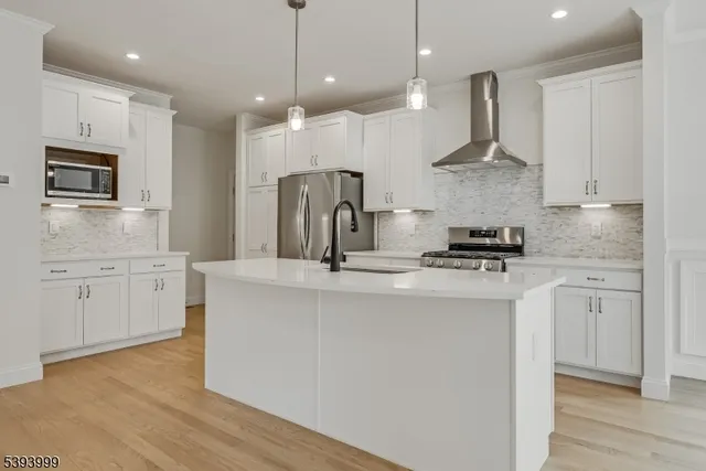 a kitchen with stainless steel appliances granite countertop a sink a stove a refrigerator and island with wooden floor