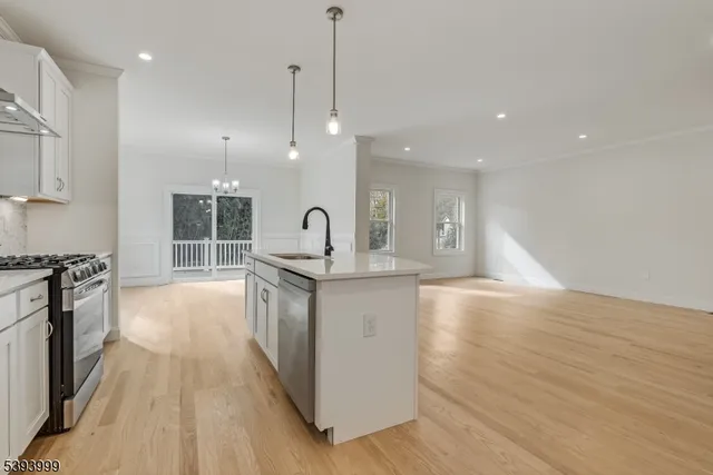 a large kitchen with stainless steel appliances a large counter top a stove a sink dishwasher a refrigerator and white cabinets with wooden floor