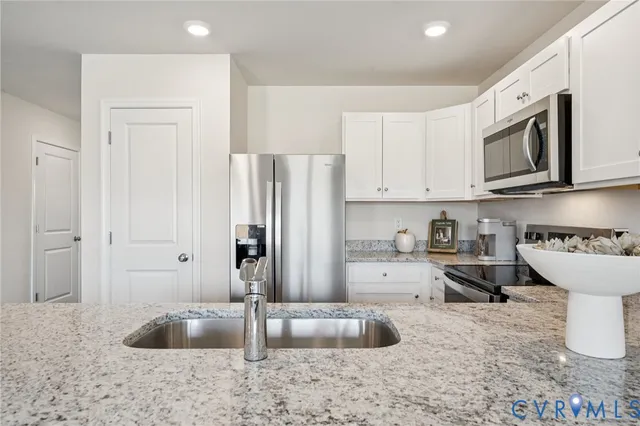 a kitchen with stainless steel appliances granite countertop a refrigerator a stove a sink and white cabinets