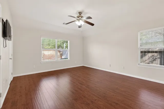 an empty room with wooden floor chandelier fan and windows
