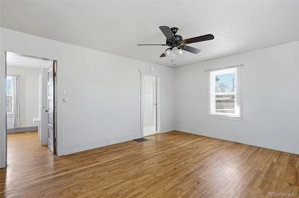 a view of an empty room with wooden floor and a ceiling fan