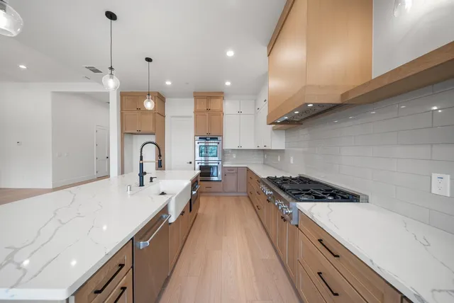 a large kitchen with stainless steel appliances a large counter top a stove and a wooden floors