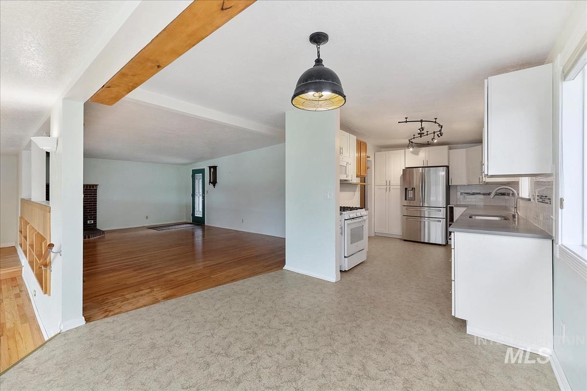 7141 West Hill Road Boise, ID 83714 - Photo 5 of 28 Modern kitchen featuring stainless steel appliances, white shaker-style cabinetry, dark countertops, a subway tile backsplash with decorative accents, and track lighting