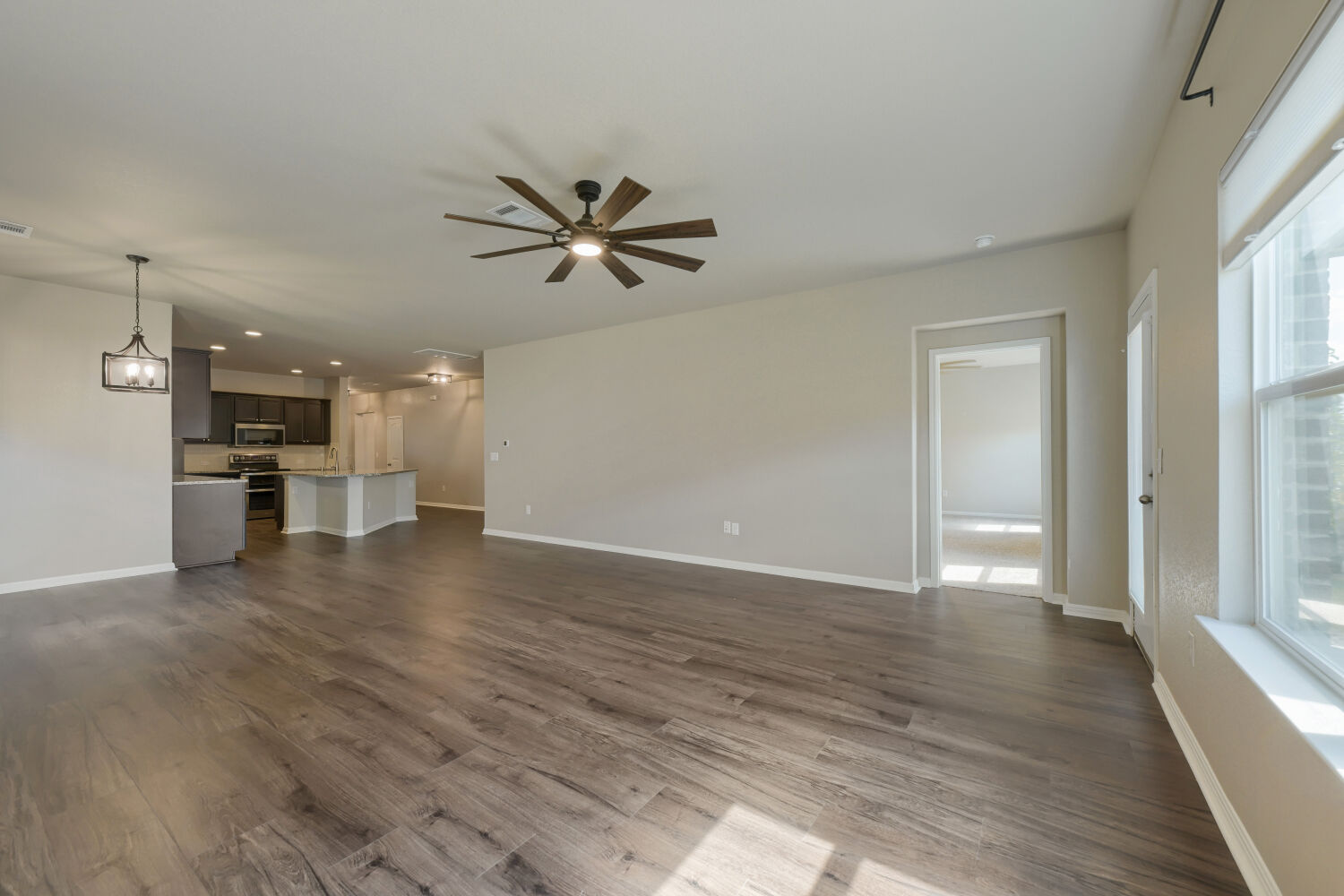Rich wood-look flooring stretches across a generous open layout illuminated by natural window light.