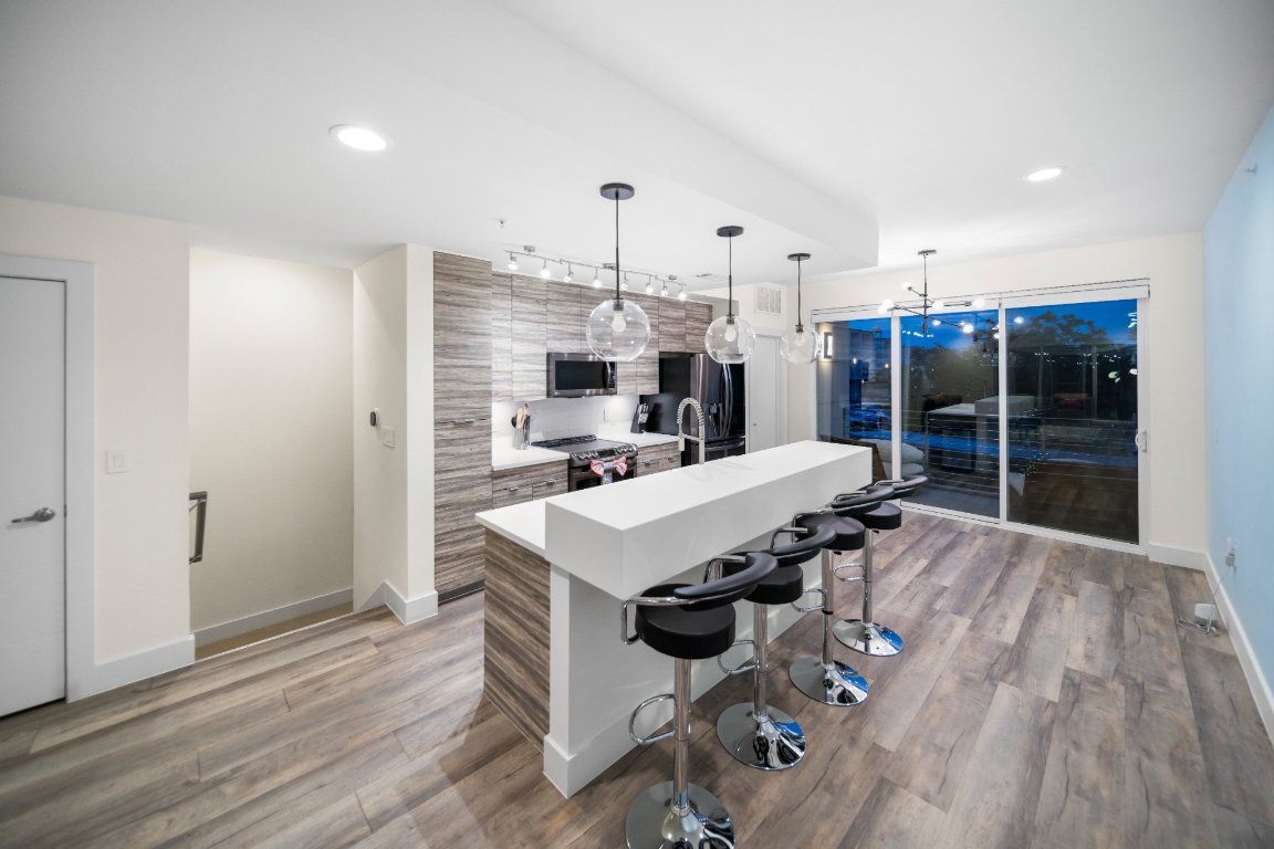 604 North Bluff Drive, Unit 247 Austin, TX 78745 - Photo 13 of 23 Kitchen with stainless steel appliances, a kitchen island with sink, wood finished floors, light countertops, and a kitchen breakfast bar