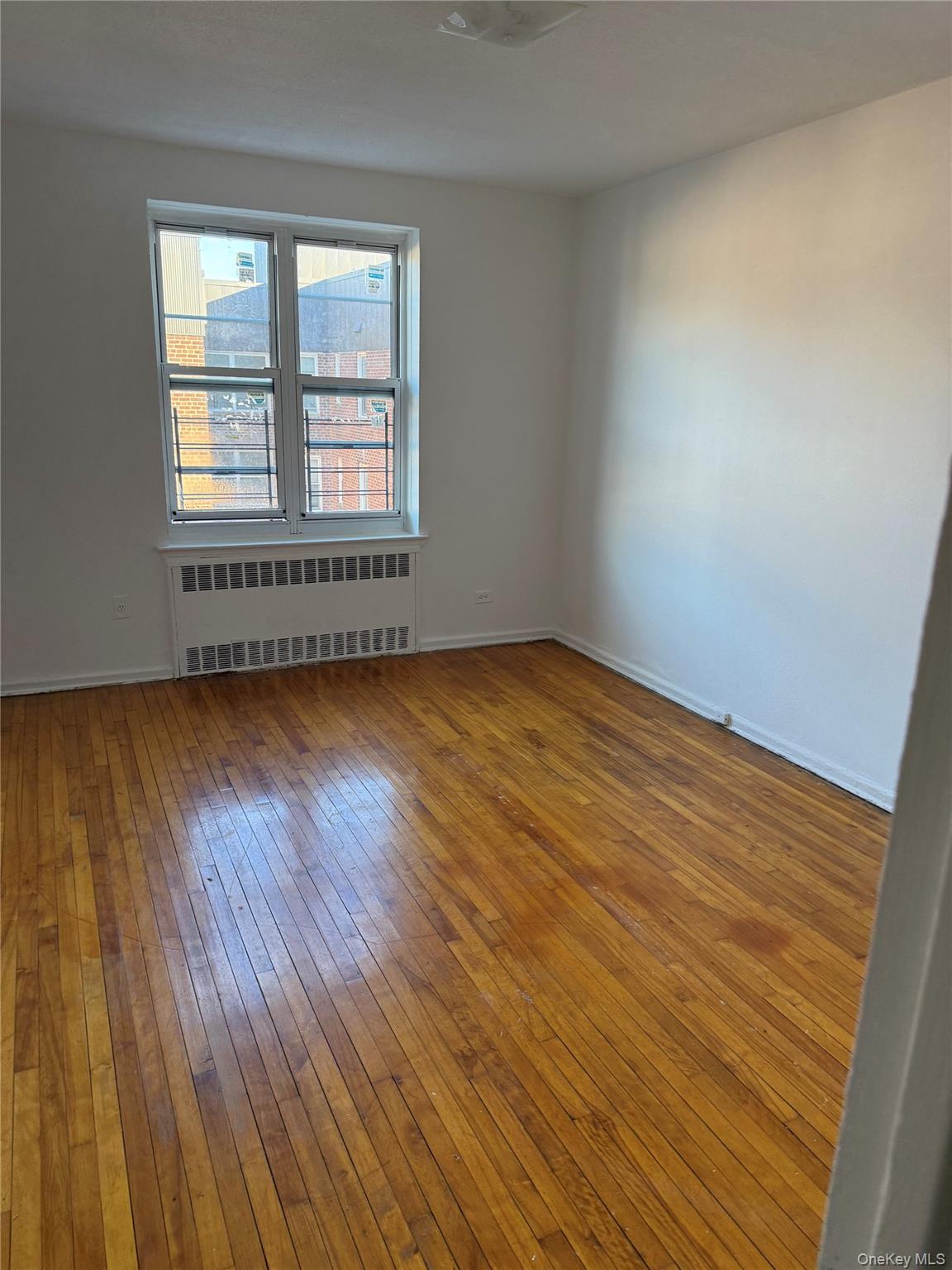 33-25 81st Street, Unit 6E Queens, NY 11372 - Photo 5 of 9 a view of an empty room with wooden floor and a window