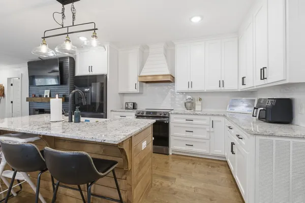 a kitchen with stainless steel appliances granite countertop a sink dishwasher a stove a refrigerator and white cabinets with wooden floor