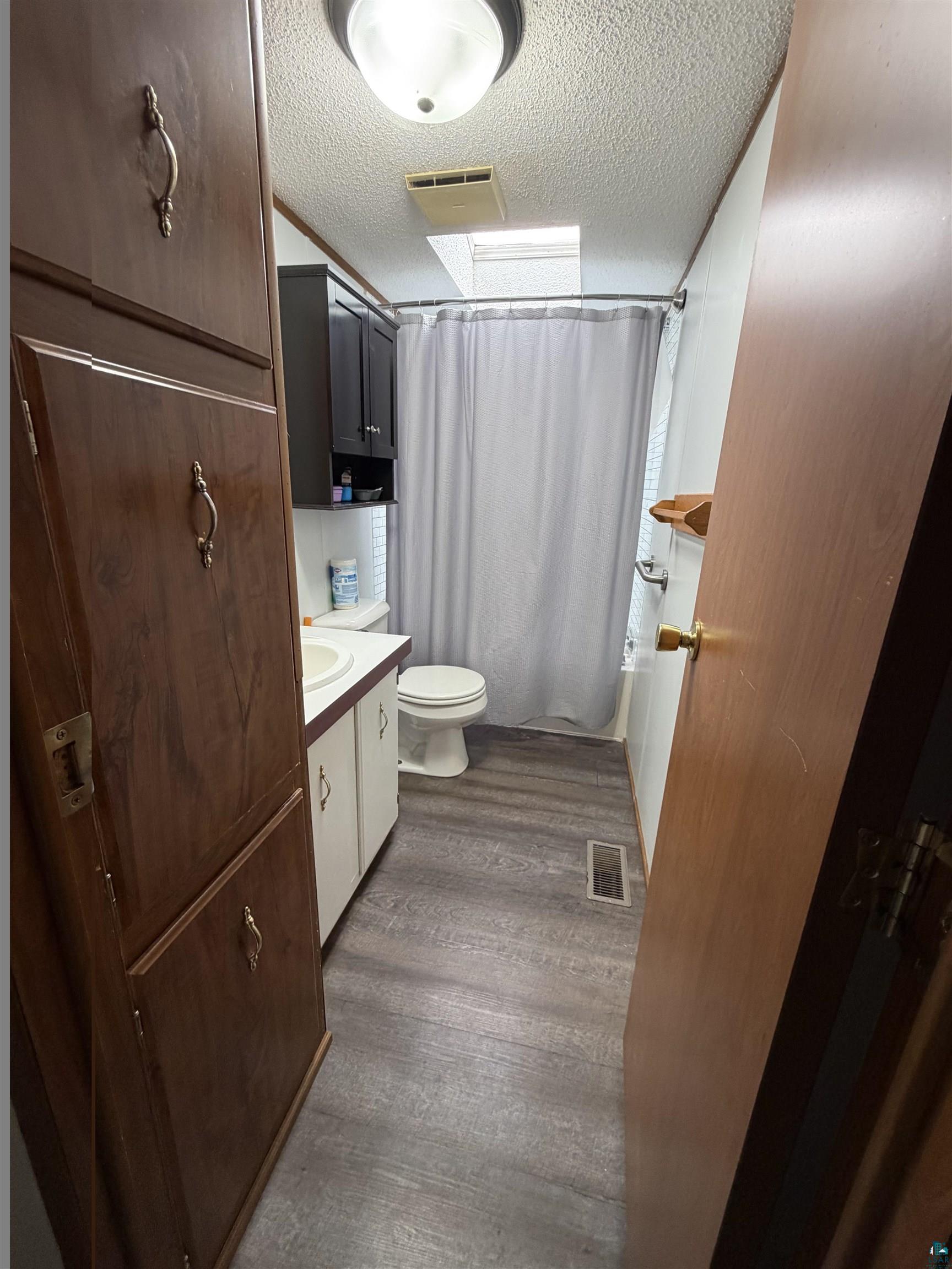 23 Juniper Lane Duluth, MN 55810 - Photo 11 of 12 Bathroom featuring wood-finish flooring, a white vanity with an integrated sink, a toilet, and a shower area with a curtain