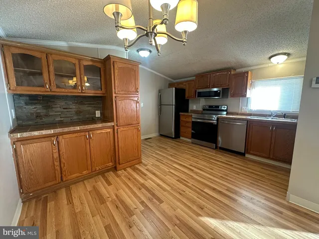 a kitchen with stainless steel appliances granite countertop a refrigerator a sink dishwasher a stove and white countertops with wooden floor