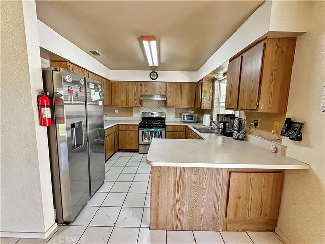 a large kitchen with stainless steel appliances a refrigerator a sink dishwasher a oven a dining table and chairs with wooden floor