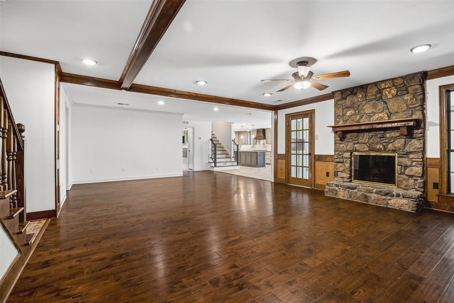 8970 Farmoor Road Germantown, TN 38139 - Photo 7 of 35 Expansive living area featuring wood-finish flooring, a stone-clad fireplace with a wood mantel, exposed ceiling beams, a ceiling fan, and French doors