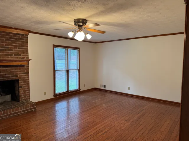 a view of an empty room with wooden floor and a fireplace