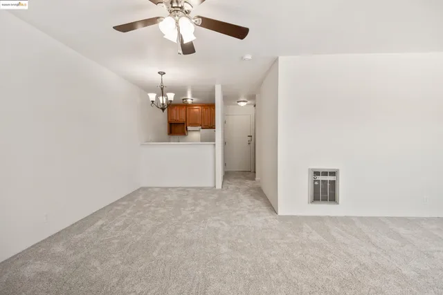 en empty room with chandelier fan and kitchen view