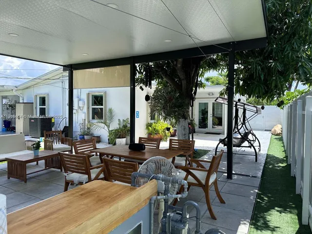 a view of a patio with dining table and chairs under an umbrella with a large tree