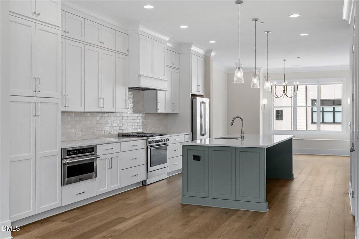 a kitchen with stainless steel appliances granite countertop a stove a sink a refrigerator and white cabinets with wooden floor