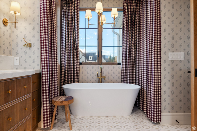558 West Rheinfalls Circle Midway, UT 84049 - Photo 20 of 61 Freestanding soaking tub with floor-mounted brass faucet, patterned floor tiling, and a wooden vanity with a light-colored countertop