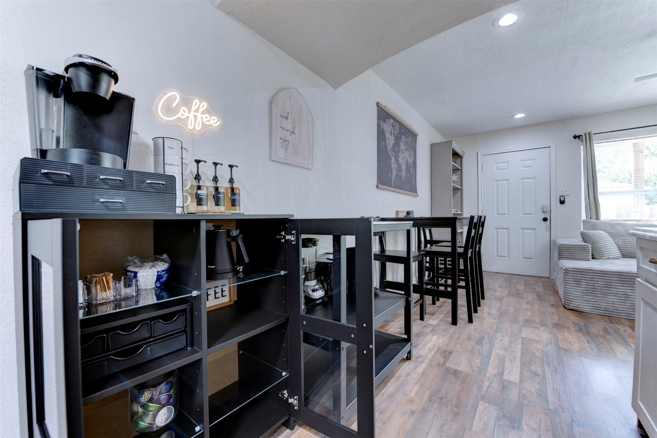 1121 Panama Street Houston, TX 77009 - Photo 16 of 35 Dining and coffee station area with wood-look LVP flooring, recessed lighting, Keurig coffee maker with syrup dispenser set, black metal storage cabinet with glass doors, black bar-height dining table with four chairs, six-panel entry door with smart lock, and oversized window with natural light.