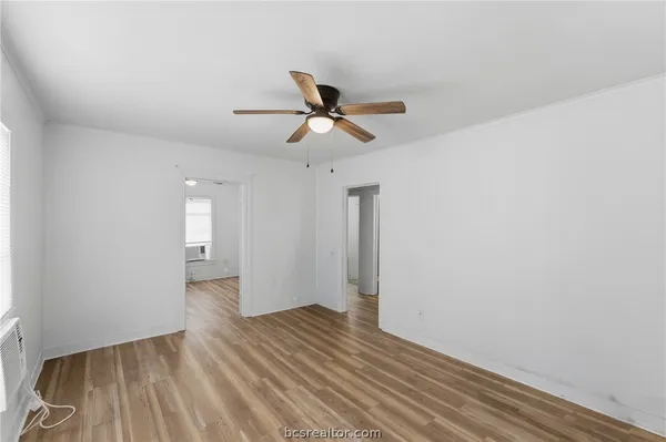 an empty room with wooden floor fan and windows