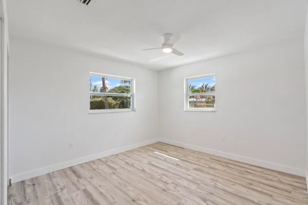 an empty room with wooden floor ceiling fan and windows