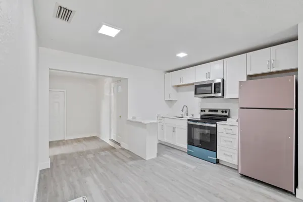 a kitchen with stainless steel appliances granite countertop a refrigerator a stove a sink dishwasher and white cabinets with wooden floor