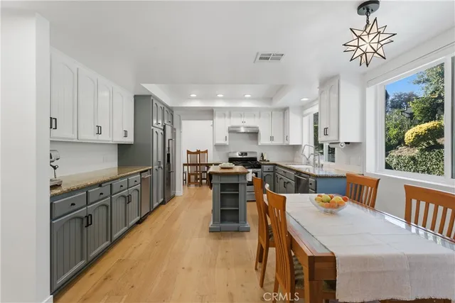 a kitchen with stainless steel appliances granite countertop a stove top oven a sink dishwasher a dining table and chairs with wooden floor