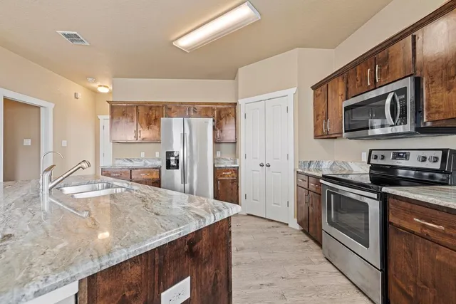 a kitchen with stainless steel appliances granite countertop a refrigerator a stove and a sink with wooden floors