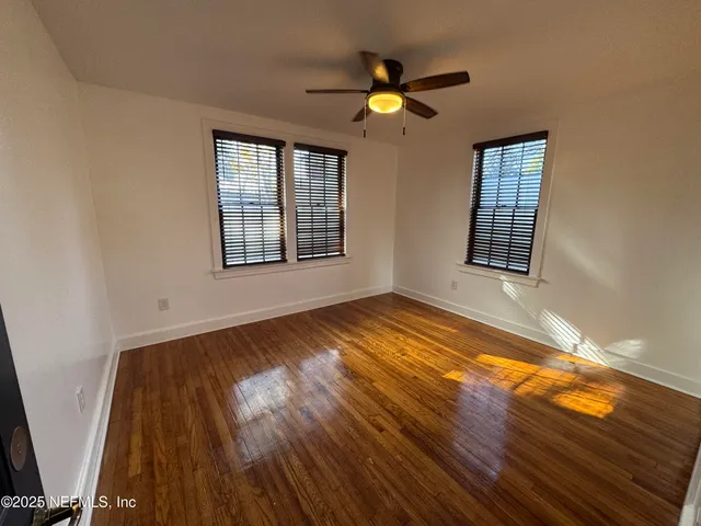 a view of empty room with wooden floor and fan