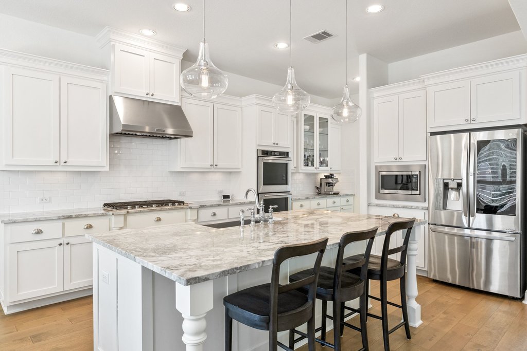 5812 Davenport Divide Road Austin, TX 78738 - Photo 16 of 40 The oversized island features substantial turned legs, polished stone counters, and a deep apron-front sink. Glass pendant lighting adds a soft architectural touch overhead.