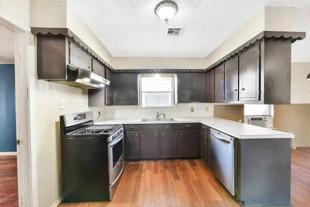 a kitchen with stainless steel appliances granite countertop a sink a stove a refrigerator cabinets and a window