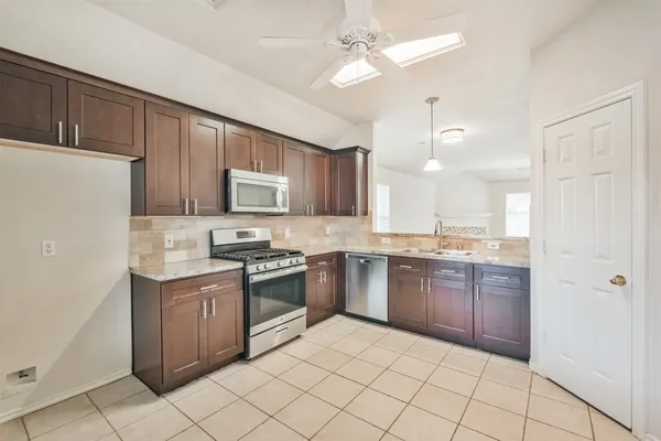 a kitchen with stainless steel appliances granite countertop a stove top oven a sink dishwasher and a refrigerator with wooden cabinets