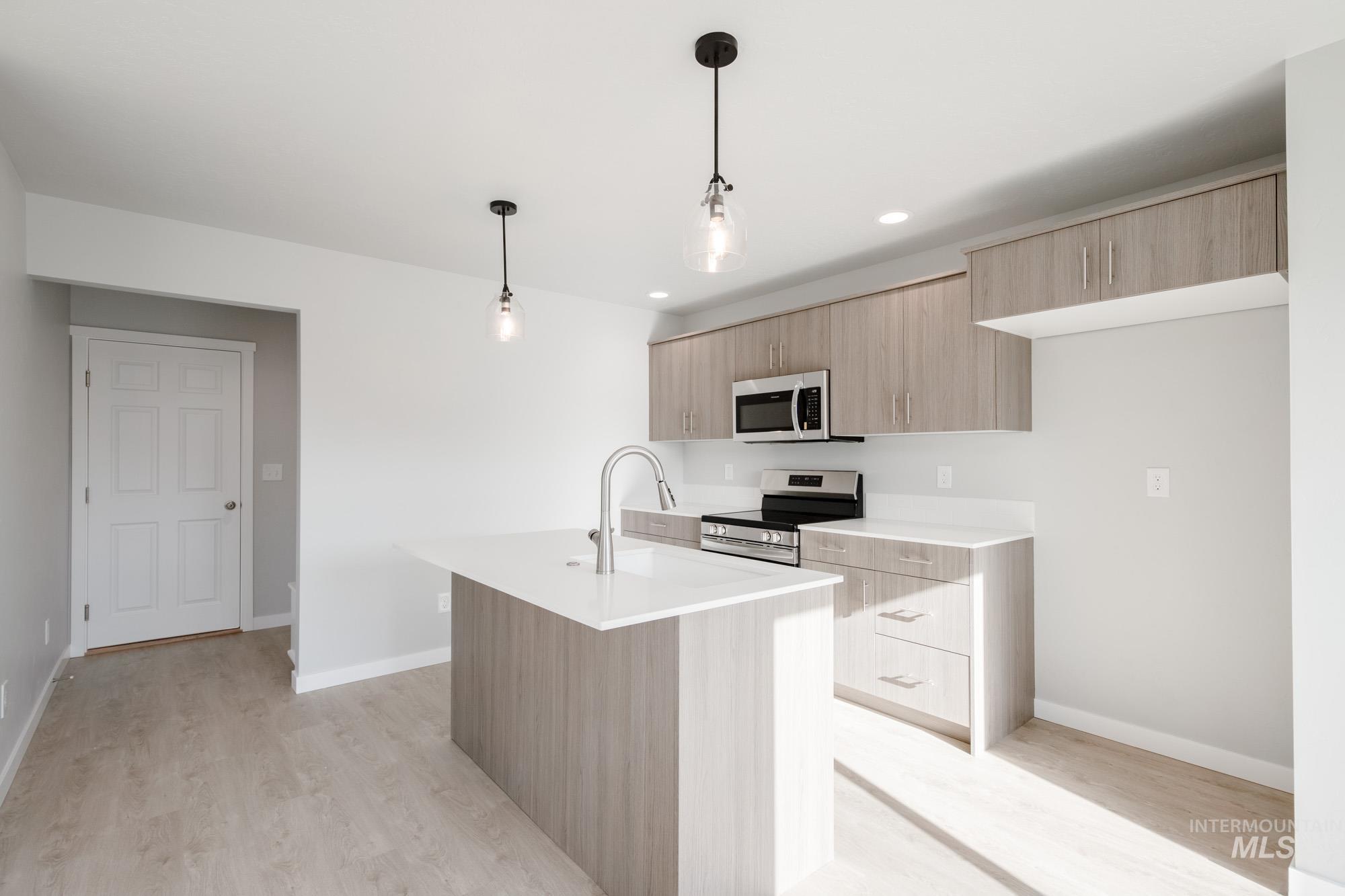 229 Moose Street Horseshoe Bend, ID 83629 - Photo 7 of 27 Kitchen with light brown cabinets, appliances with stainless steel finishes, decorative light fixtures, light wood-style flooring, and a center island with sink