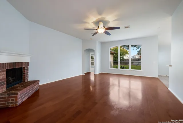 an empty room with windows fireplace and a kitchen view