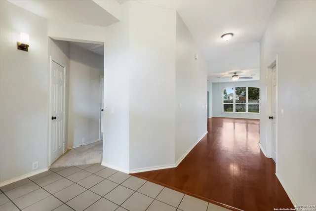 a view of a hallway to an empty room with wooden floor and a window