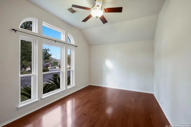 an empty room with wooden floor chandelier fan and windows