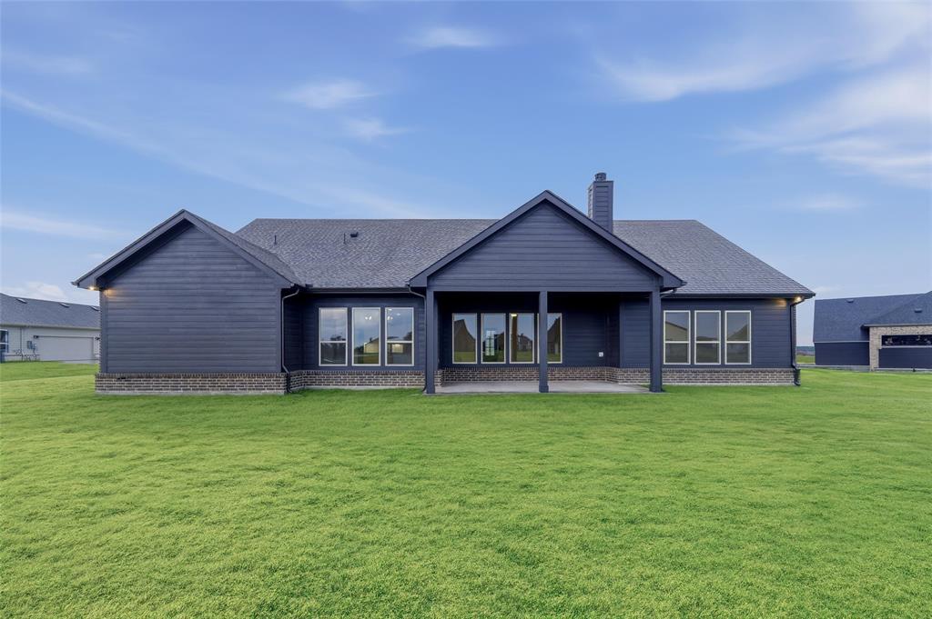 2208 Continent Court Krum, TX 76249 - Photo 24 of 26 Expansive green lawn bordering the rear elevation featuring dark siding and a covered patio