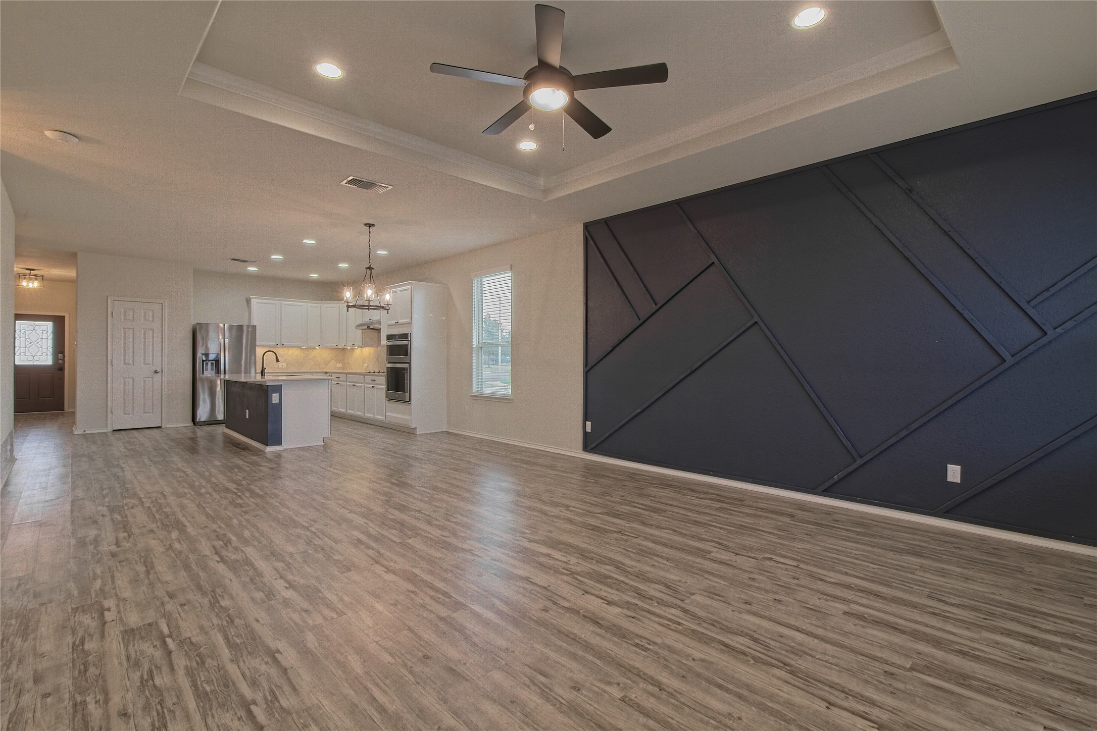 601 Hummingbird Lane Leander, TX 78641 - Photo 12 of 35 Unfurnished living room featuring ceiling fan, a decorative wall, dark wood-style flooring, a tray ceiling, and a chandelier
