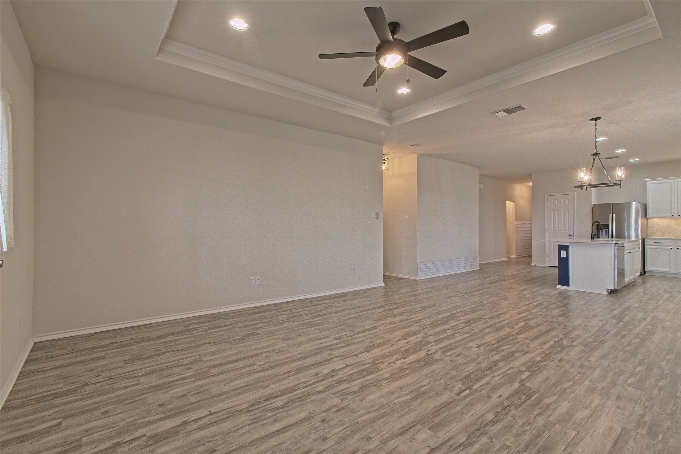 601 Hummingbird Lane Leander, TX 78641 - Photo 14 of 35 Unfurnished living room featuring ceiling fan, light wood-style floors, hanging lights, crown molding, and a tray ceiling