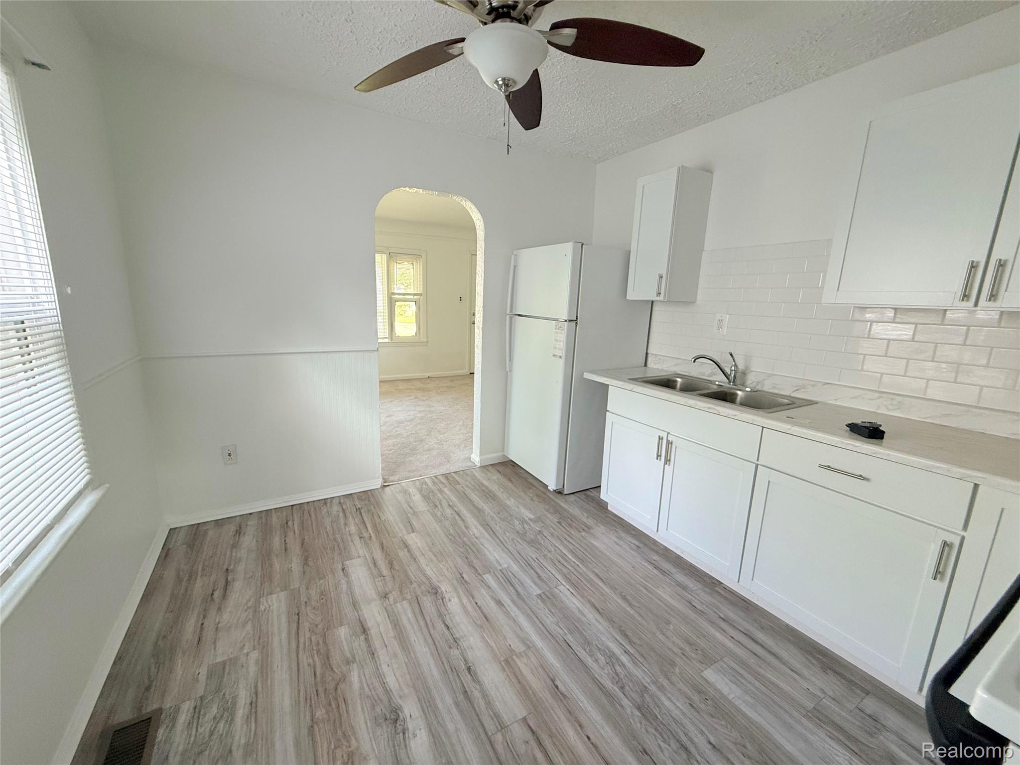 21212 Rensselaer Street Farmington, MI 48336 - Photo 5 of 11 Contemporary kitchen featuring wood-finish flooring, white cabinetry, a dual basin stainless steel sink, subway tile backsplash, and a white refrigerator