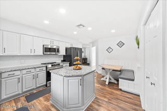 a kitchen with stainless steel appliances granite countertop a stove top oven a sink dishwasher and white cabinets with wooden floor