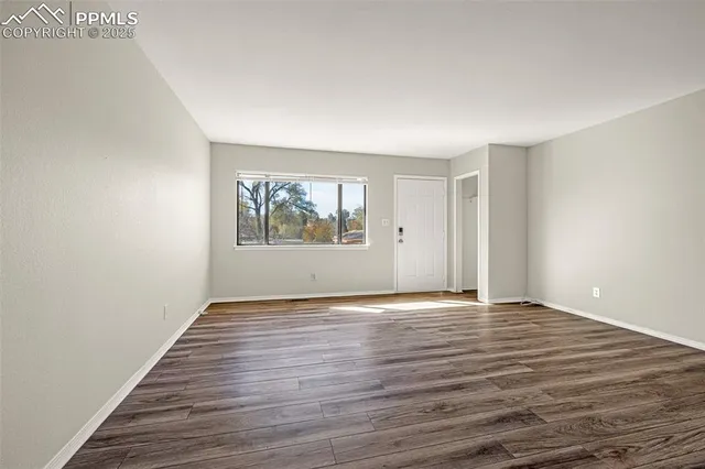 a view of an empty room with wooden floor and a window