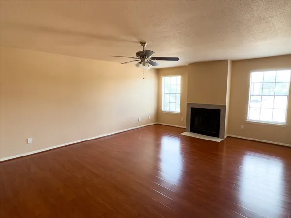 an empty room with wooden floor fan and windows