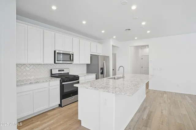 a kitchen with stainless steel appliances granite countertop a sink dishwasher a stove and a refrigerator with wooden floor