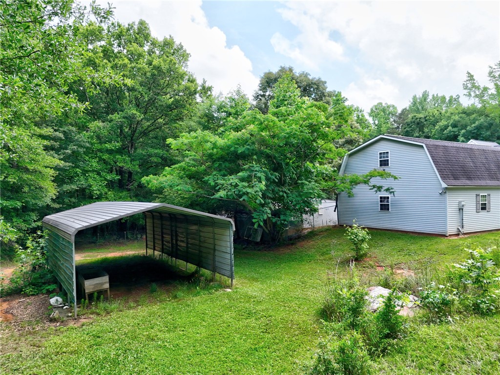 1016 Campbell Road Belton, SC 29627 - Photo 46 of 50 A spacious backyard with a barn-style structure and an open carport, nestled among verdant trees.