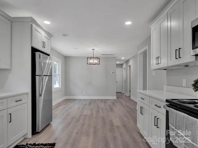 a kitchen with stainless steel appliances granite countertop a refrigerator a stove and white cabinets with wooden floors