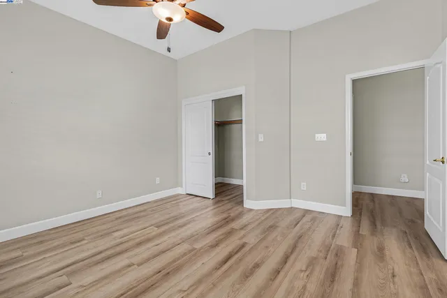 a view of an empty room with wooden floor closet and a ceiling fan