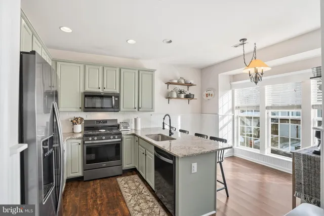 a kitchen with stainless steel appliances granite countertop a stove a sink dishwasher a refrigerator and white cabinets with wooden floor